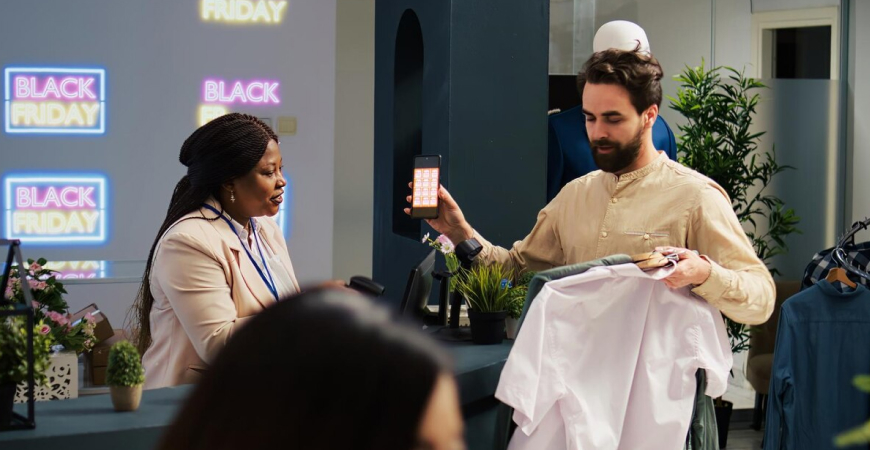 Black Friday no comércio do ABC — vendedora mostrando produto e maquininha para cliente em loja decorada com letreiros da Black Friday